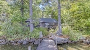 A wooden dock leading to a house surrounded by trees and a clear stream. - Squam Lake House - Lakeside With Private Dock and Float (Holderness)