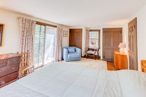 Ein Schlafzimmer mit einem Bett, einem Holzkleiderschrank, einem blauen Sessel, einem Nachttisch mit Lampe und einer Holzkommode.