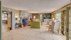 A spacious living room with a fireplace, a dining area, and a library. - Squam Lake House - Lakeside With Private Dock and Float (Holderness)