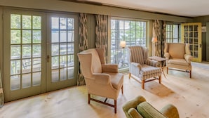 A room with a large sliding glass door, a patterned armchair, a striped armchair, a small table, and a green sofa. - Squam Lake House - Lakeside With Private Dock and Float (Holderness)
