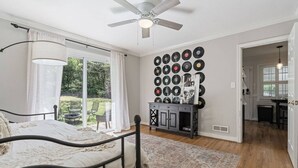 Ein Schlafzimmer mit Bett, Deckenventilator, einer Wand voller Schallplatten und Blick ins Freie.