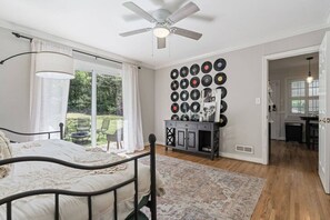 Ein Schlafzimmer mit Bett, Deckenventilator, einer Wand voller Schallplatten und Blick ins Freie.