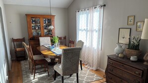 Un coin repas comprenant une table en bois, des chaises, un meuble avec des portes en verre, une plante en pot et une fenêtre avec des rideaux.