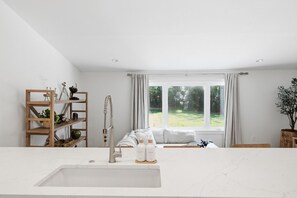 Eine moderne Küche mit einem großen Fenster, einem Holzbodenregal und einer Marmorarbeitsplatte.