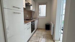 A compact kitchen with white cabinets, a window, and a tiled floor. - Le Rempart - Terrasse - Centre-ville (Niort)