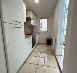 Une cuisine de taille réduite avec des meubles blancs, une fenêtre et un sol carrelé.