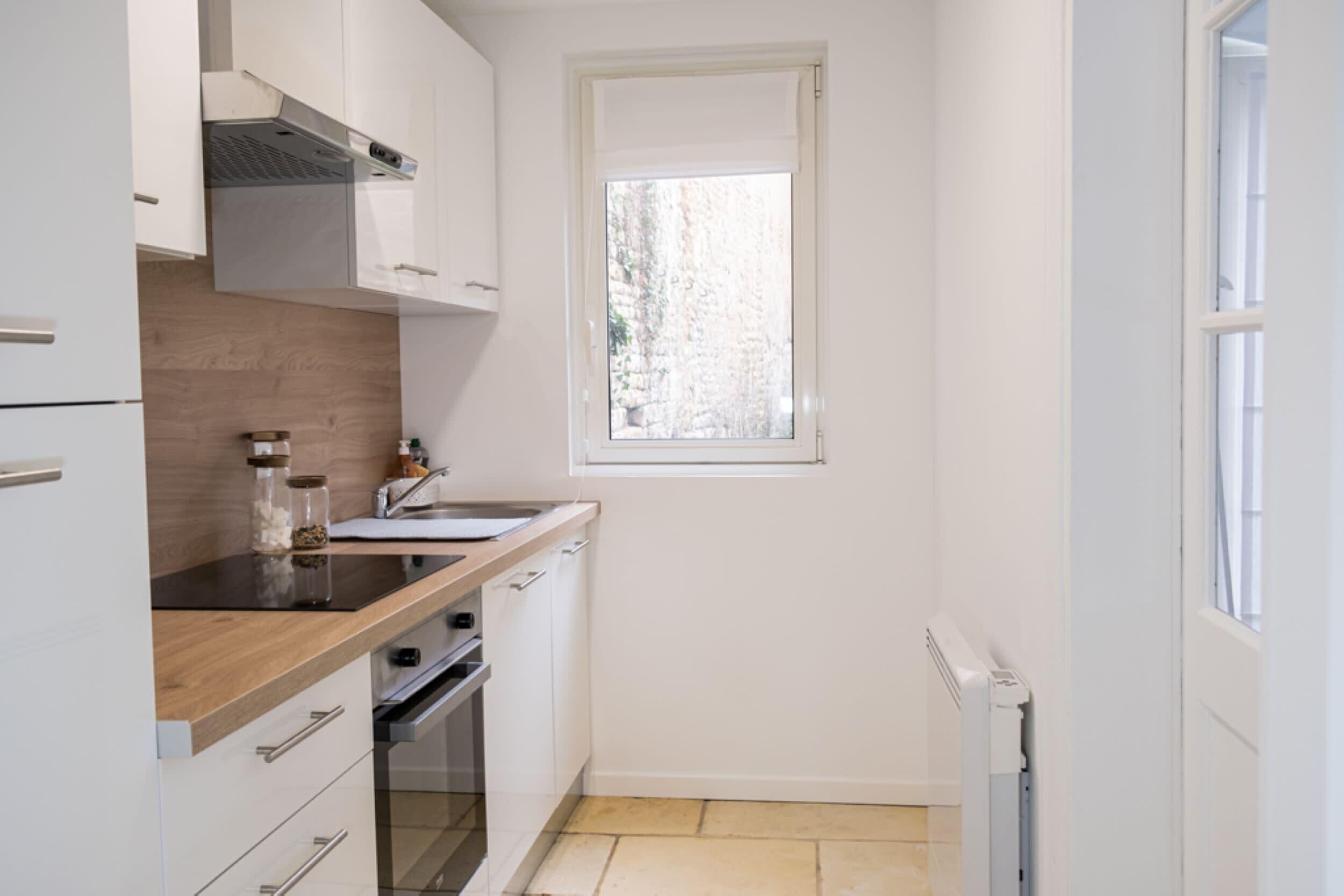 Eine kleine Küche mit weißen Schränken, einer Holz Arbeitsplatte, einem Fenster und einem eingebauten Backofen.