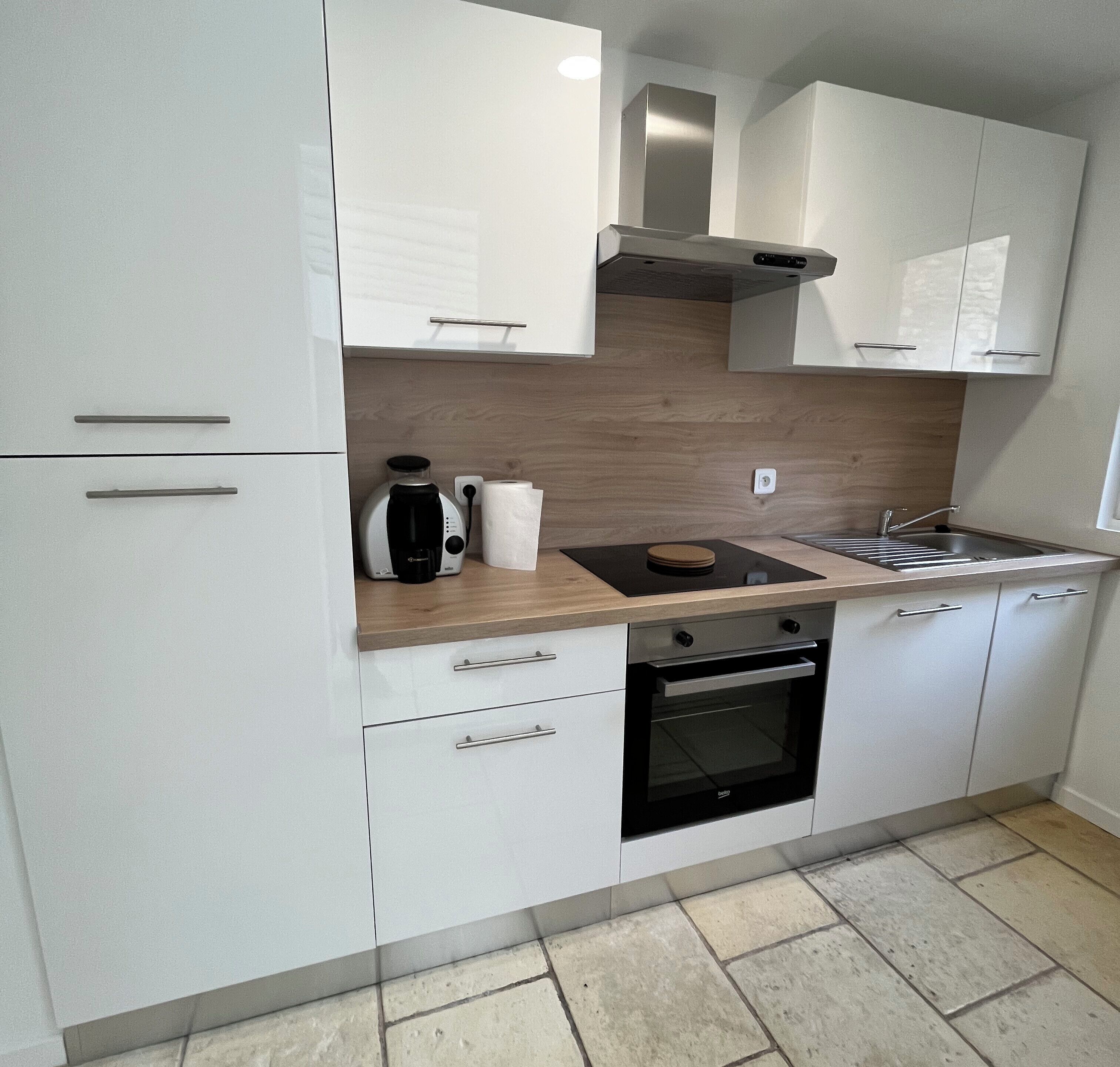 A modern kitchen with white cabinets, a built-in oven, a coffee maker, and a sink.