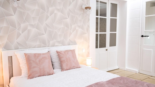 A bed with a headboard, a wall with a geometric pattern, a door, and a nightstand with a lamp. - Le Rempart - Terrasse - Centre-ville (Niort)