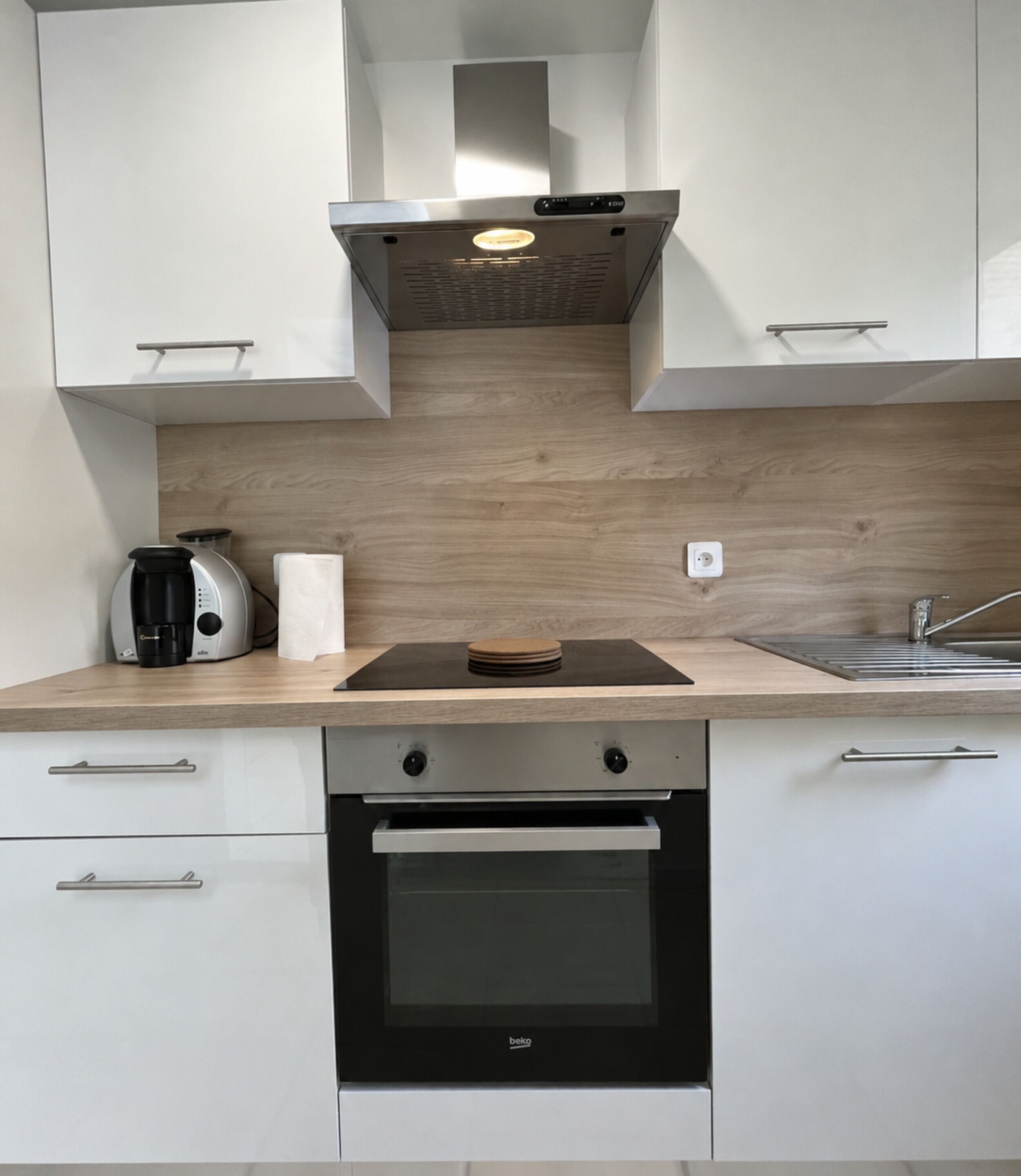 Een moderne keuken met witte kasten, een ingebouwde oven, een koffiezetapparaat en een houten spatwand.