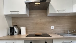 A modern kitchen with white cabinets, a built-in oven, a coffee maker, and a wooden backsplash. - Le Rempart - Terrasse - Centre-ville (Niort)