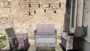 Wicker furniture with cushions, a stone wall, and a window. - Le Rempart - Terrasse - Centre-ville (Niort)