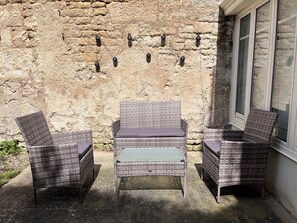 Des meubles en osier agrémentés de coussins, un mur en pierre et une fenêtre.