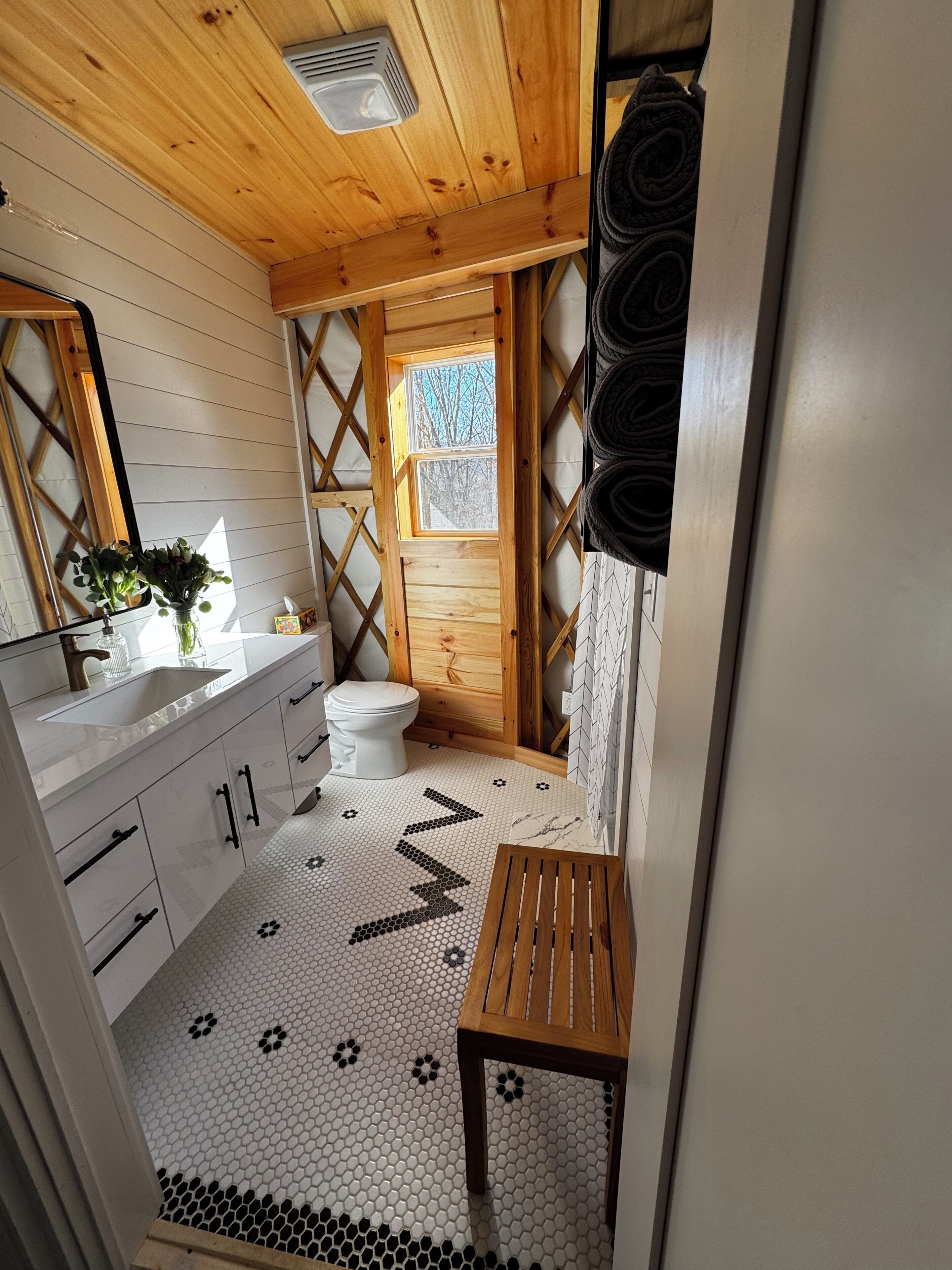 Une petite salle de bain avec un plafond en bois, un lavabo blanc, des toilettes et un petit banc en bois.