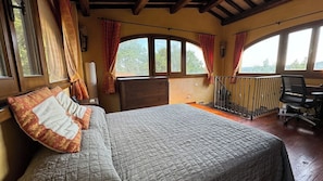 A bedroom with a bed, a desk, and a balcony.