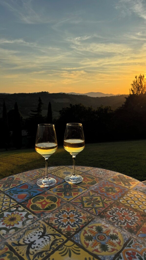 Two wine glasses on a table with a colorful pattern, set against a sunset background.