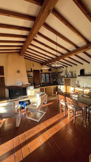 Uma cozinha ampla com vigas de madeira, lareira e área de jantar com cadeiras modernas.