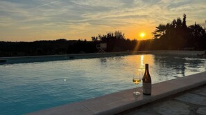 A swimming pool at sunset with a bottle and glass on the edge.