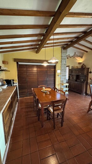 A dining area with a wooden table and chairs, a kitchen in the background, and a stone wall. - Magical Umbrian Villa with pool! (MONTECASTRILLI)