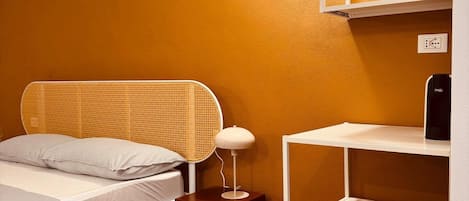 Un dormitorio con cama, mesita de noche, lámpara y una estantería blanca.