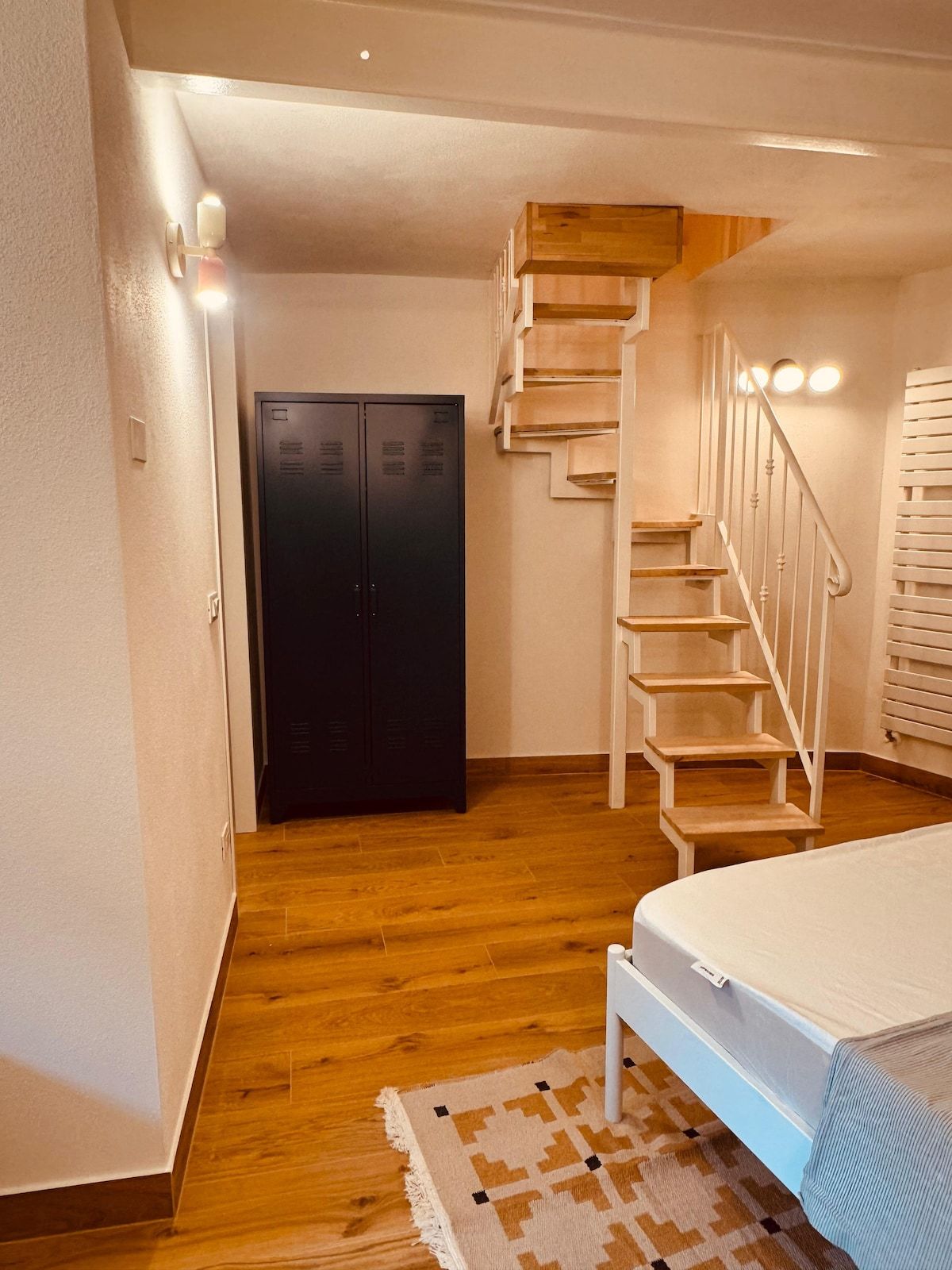 Une chambre à coucher avec un lit, un escalier en bois, une armoire et un tapis à motifs.