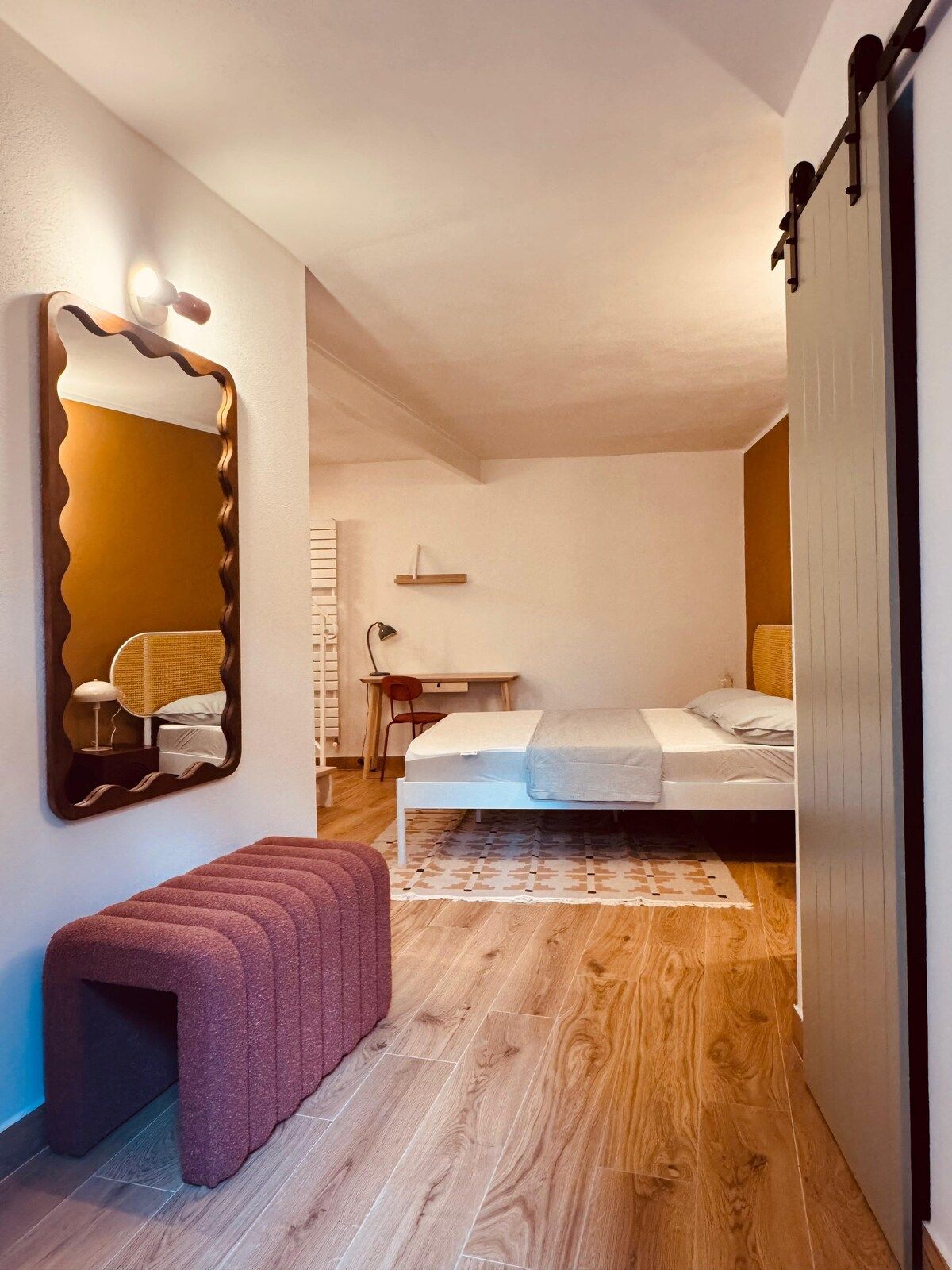 Una camera da letto con un letto, una scrivania, una sedia, uno specchio e una panca.