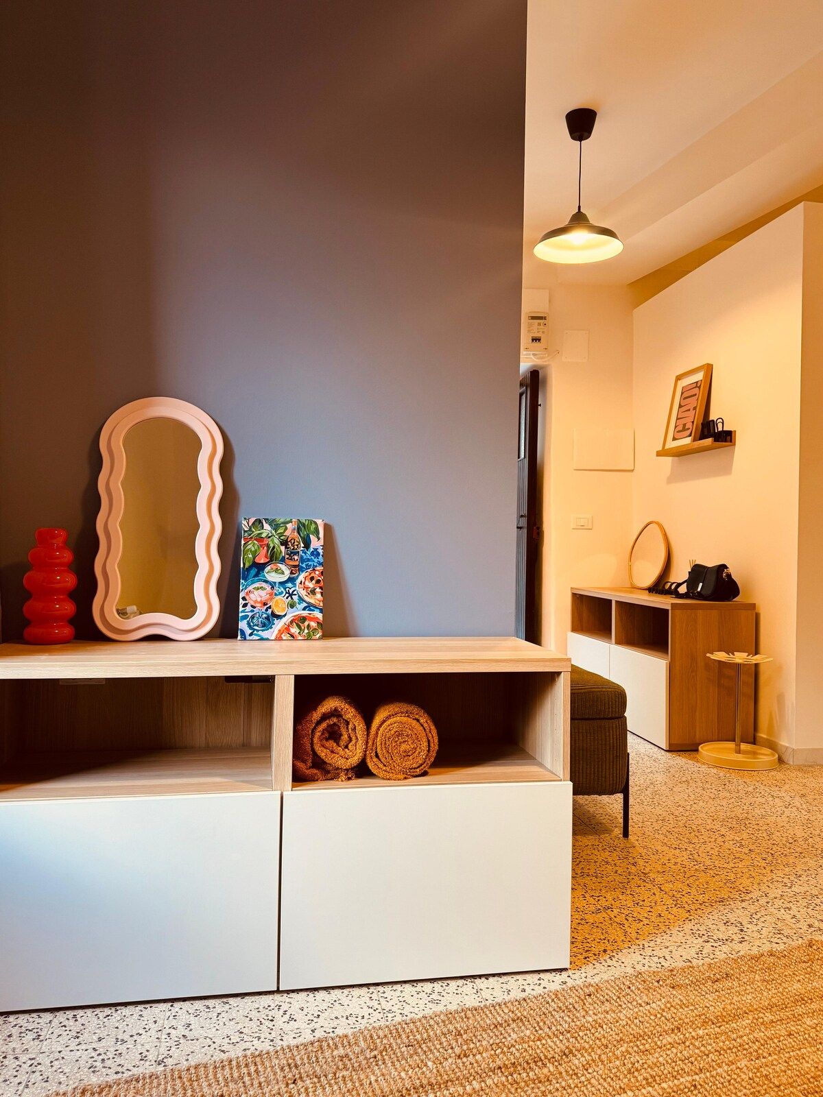 Un interno moderno con una consolle bianca, uno specchio, un'opera d'arte colorata e uno scaffale in legno con una cornice.