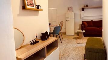 Un ambiente compatto con angolo cottura, zona pranzo e salotto con divano rosso.