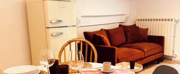 Une pièce compacte comprenant un coin cuisine, un canapé marron, une table à manger avec des verres à vin et une chaise.
