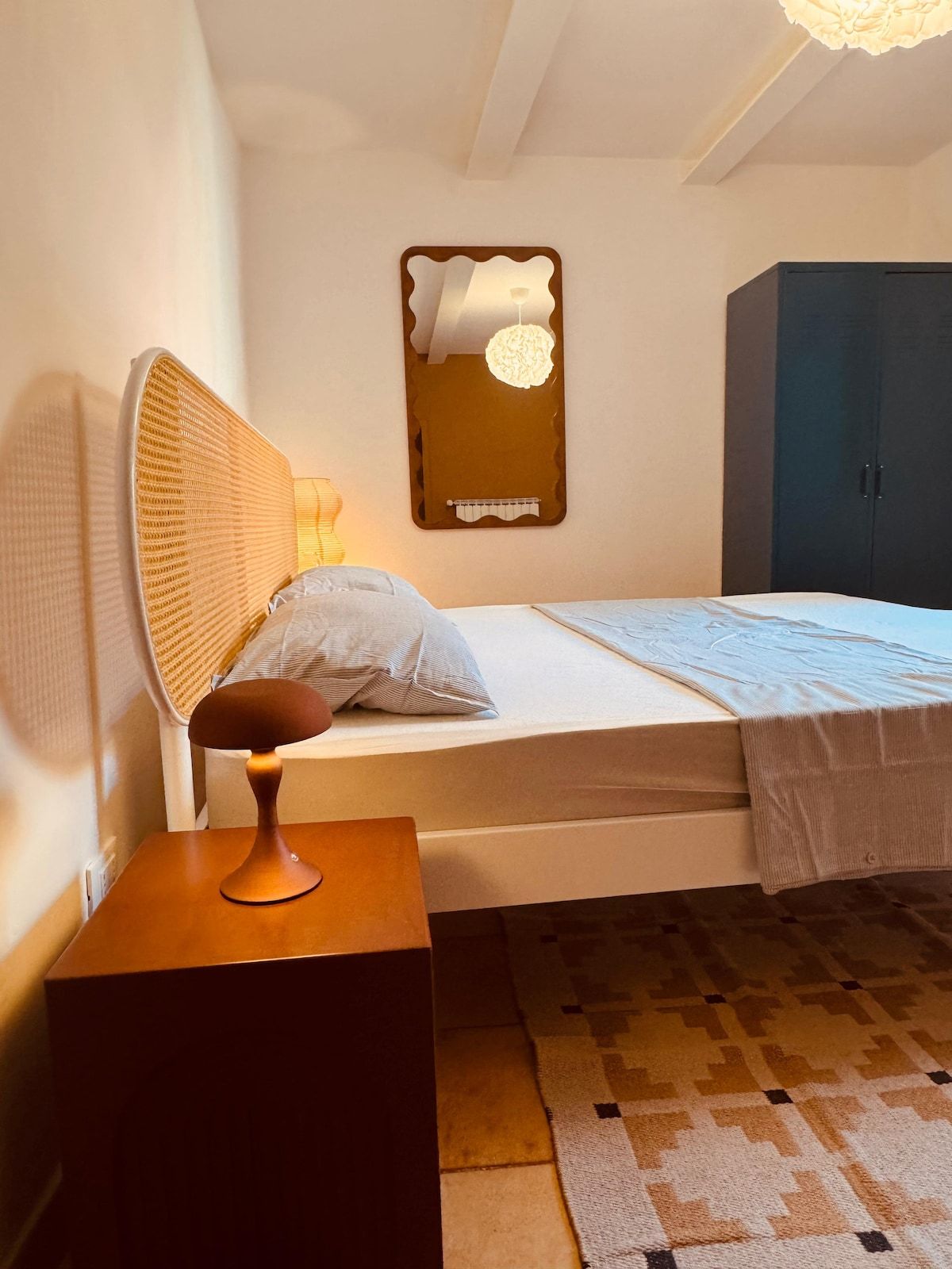 A bedroom with a single bed, a bedside table, a lamp, a mirror, and a wardrobe.