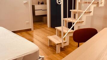 Een slaapkamer met een bed, bureau, stoel, een trap en een badkamer zichtbaar door een geopende deur.