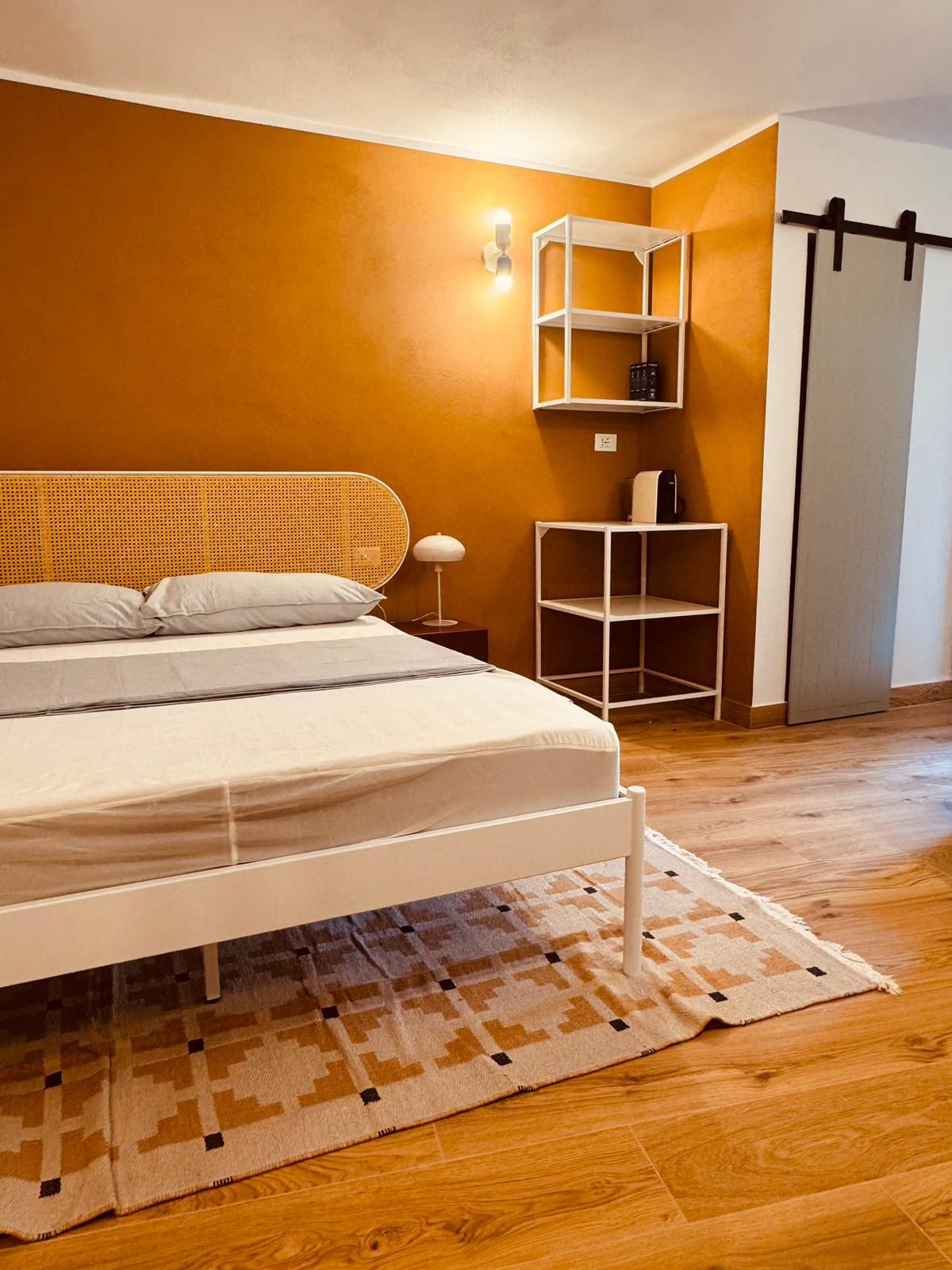 A bedroom with a bed, a nightstand, a wall-mounted shelf, and a door.