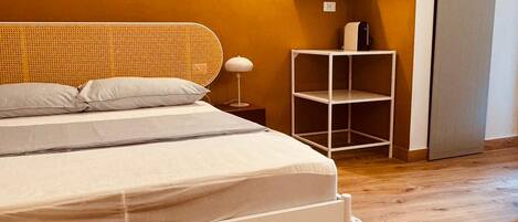 A bedroom with a bed, a nightstand, a wall-mounted shelf, and a door.