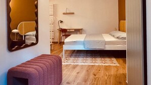 Een slaapkamer met een bed, een bureau, een stoel, een bankje, een grote spiegel en een kledingkast.