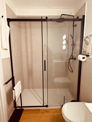 Dusche mit Glastür, Toilette und Handtuchhalter.