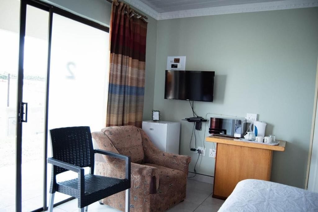 A hotel room with a bed, a desk with a microwave, a television, and a chair.