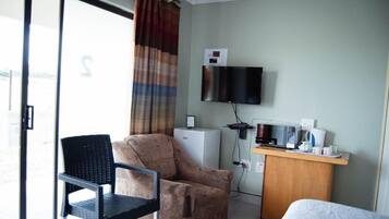 A hotel room with a bed, a desk with a microwave, a television, and a chair.