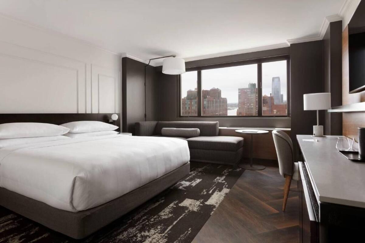 A modern hotel room with a large bed, a seating area, a small table, and a city view.