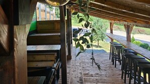 A wooden deck with benches and tables, a hanging light fixture, and a view of a green landscape. - Srce Kamene Gore – peaceful mountain retreat with spa & nature. (Kamena Gora)