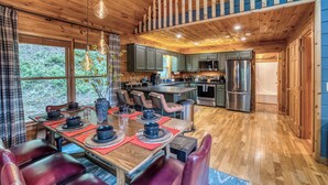 A wooden interior with a dining area, kitchen, and large windows. - Blue Bear Cabin | Views + Hot Tub + Sports Court (Blue Ridge)