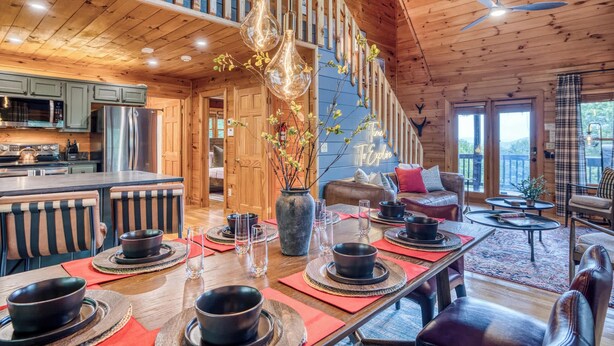 A wooden interior with a dining area, kitchen, and a staircase. - Blue Bear Cabin | Views + Hot Tub + Sports Court (Blue Ridge)