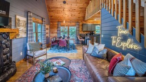 A cozy cabin interior with a dining area, a living room with a leather sofa, a staircase, and a kitchen. - Blue Bear Cabin | Views + Hot Tub + Sports Court (Blue Ridge)