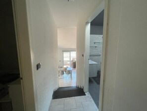 Ein Flur, der zu einem Badezimmer mit Dusche, Toilette und Waschbecken führt.