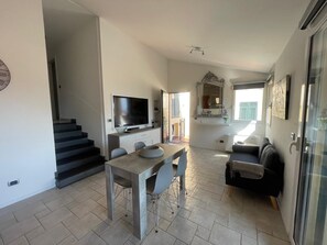 Ein modernes Interieur mit Essbereich, Flachbildfernseher, Treppe und Wohnbereich mit Sofa und Fenster.