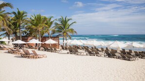 Ein Strand mit Liegestühlen, Sonnenschirmen und Palmen.