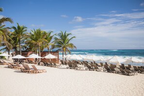 A beach with sun loungers, umbrellas, and palm trees. - Cana Rock Star/Golf and Pool/Hard Rock Area (Punta Cana)
