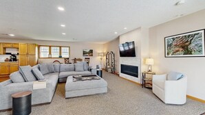 Ein Wohnzimmer mit Ecksofa, Kamin, Fernseher und einer Küche im Hintergrund.