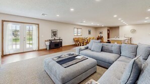Ein geräumiges Wohnzimmer mit einem grauen Ecksofa, einem Essbereich mit Holzmöbeln und einer Küche mit weißer Arbeitsplatte.
