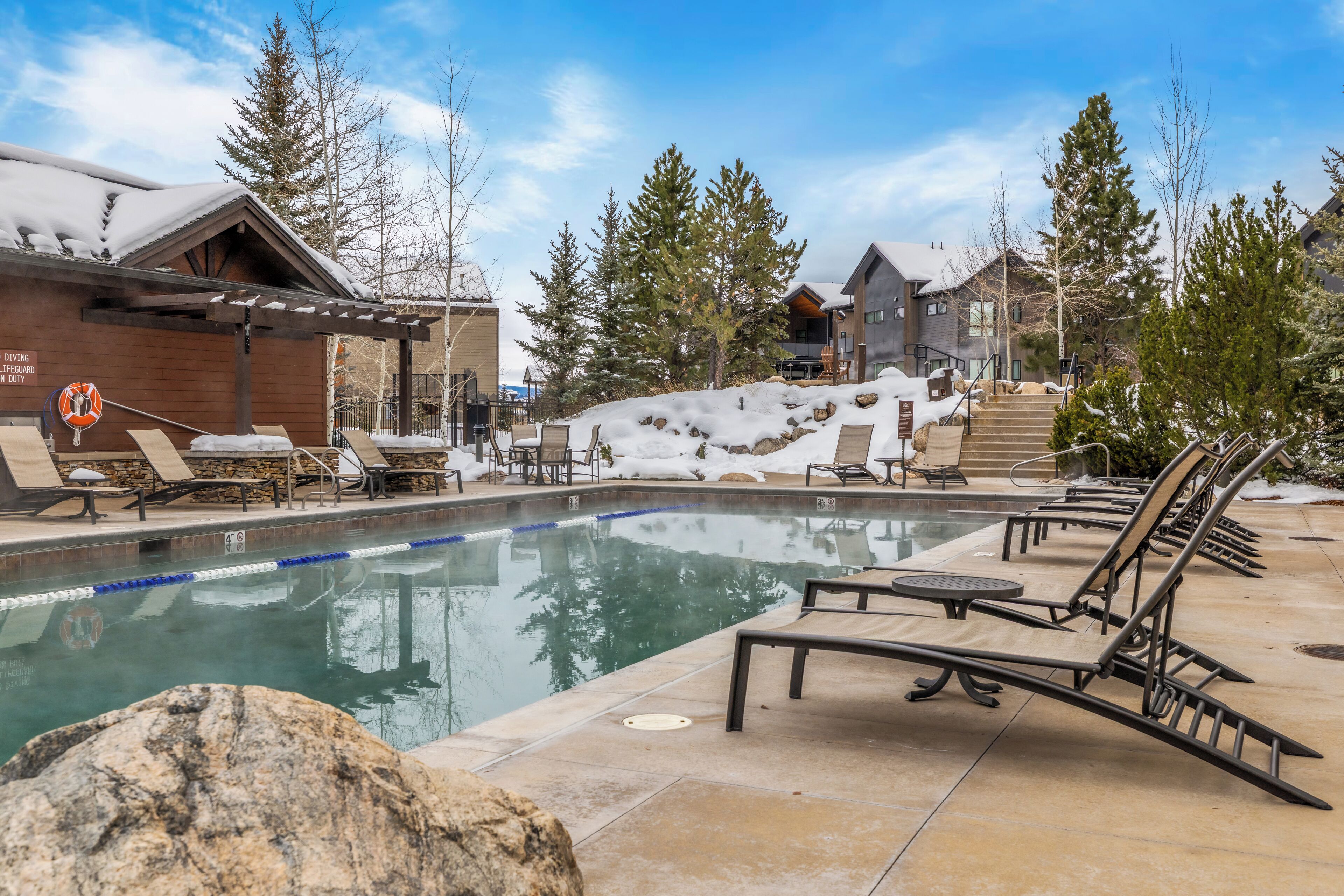Un espace piscine doté de chaises longues et d’un jacuzzi, entouré d’escaliers et d’arbres recouverts de neige.