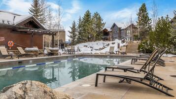 Un espace piscine doté de chaises longues et d’un jacuzzi, entouré d’escaliers et d’arbres recouverts de neige.
